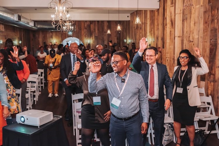 loan readiness program Culturally Responsive Support A diverse group of people, including Black and white professionals, at a business workshop, smiling and raising their hands.