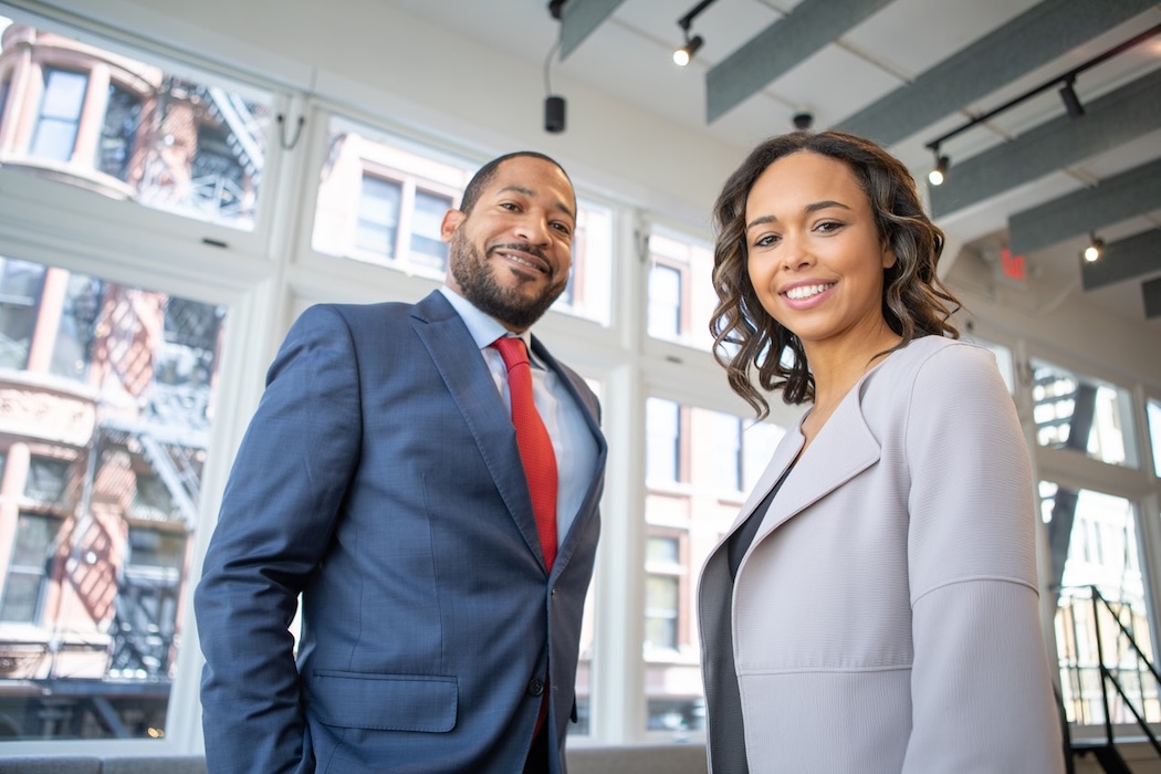 loan readiness program Institutional Trust & Reach Two Black professionals, a man and a woman, smiling and standing in a modern office with large windows overlooking a city street